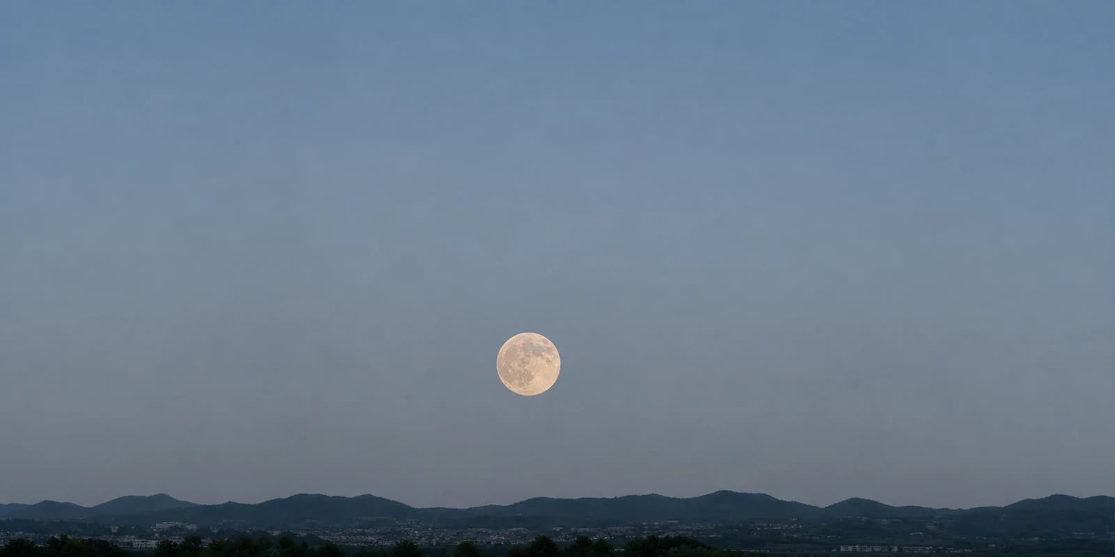 夏の宵、山並みの上の低い空に浮かぶ満月