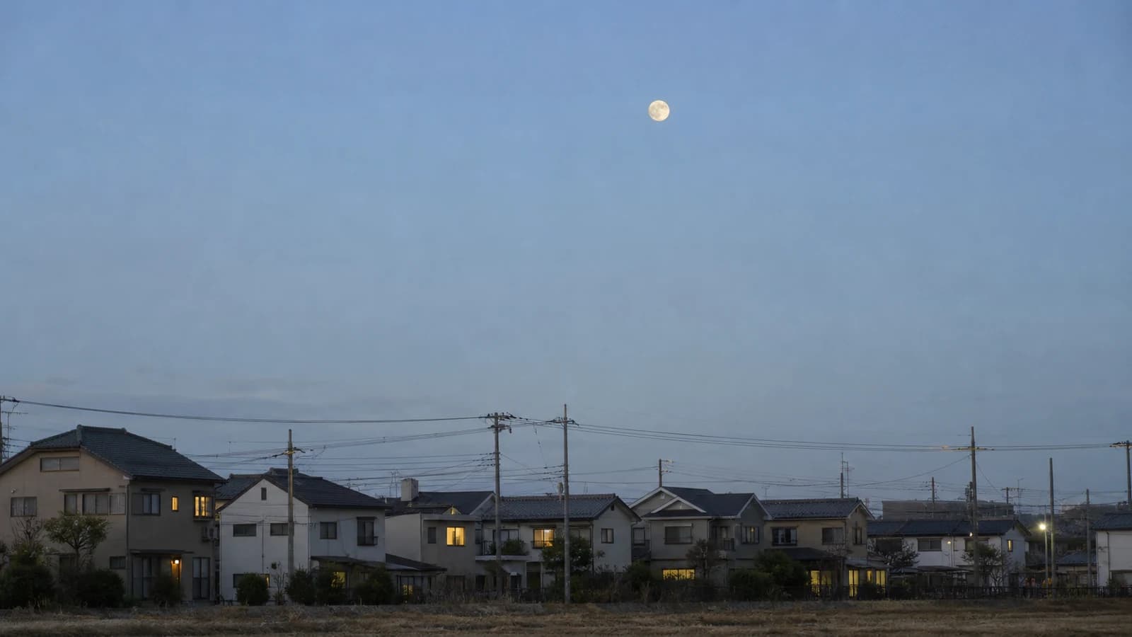住宅街の屋根の上、高く晴れた冬空に見える満月