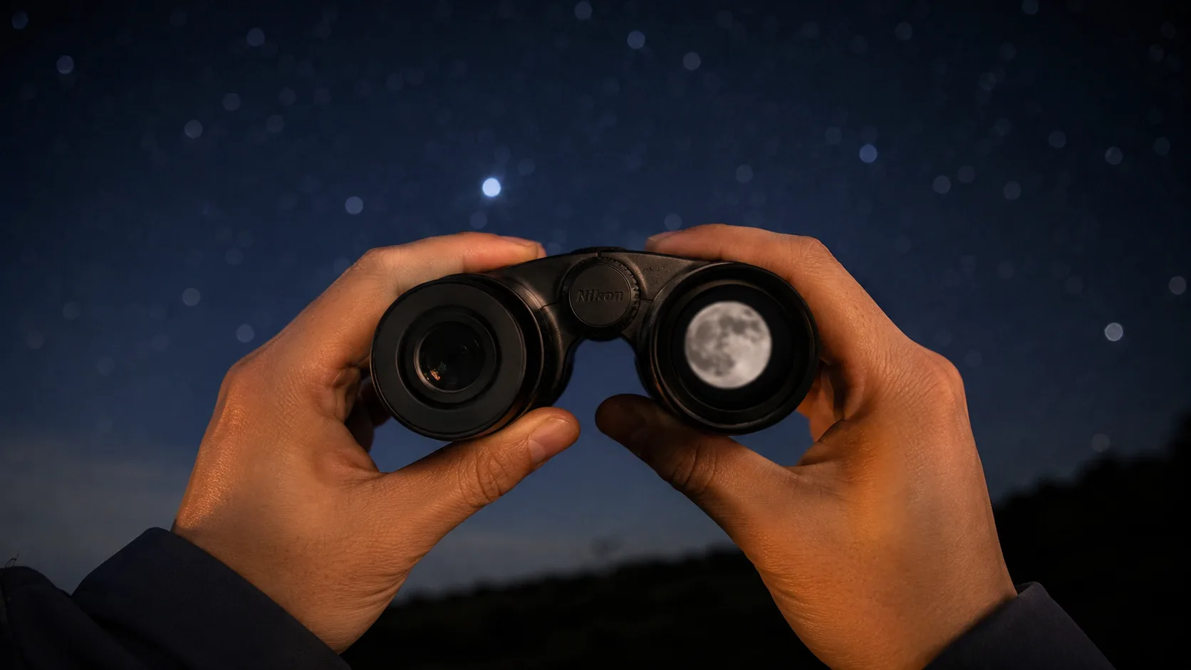 星空の下で両手に双眼鏡を構える様子。片方の対物レンズ越しに月が大きく映って見えている。