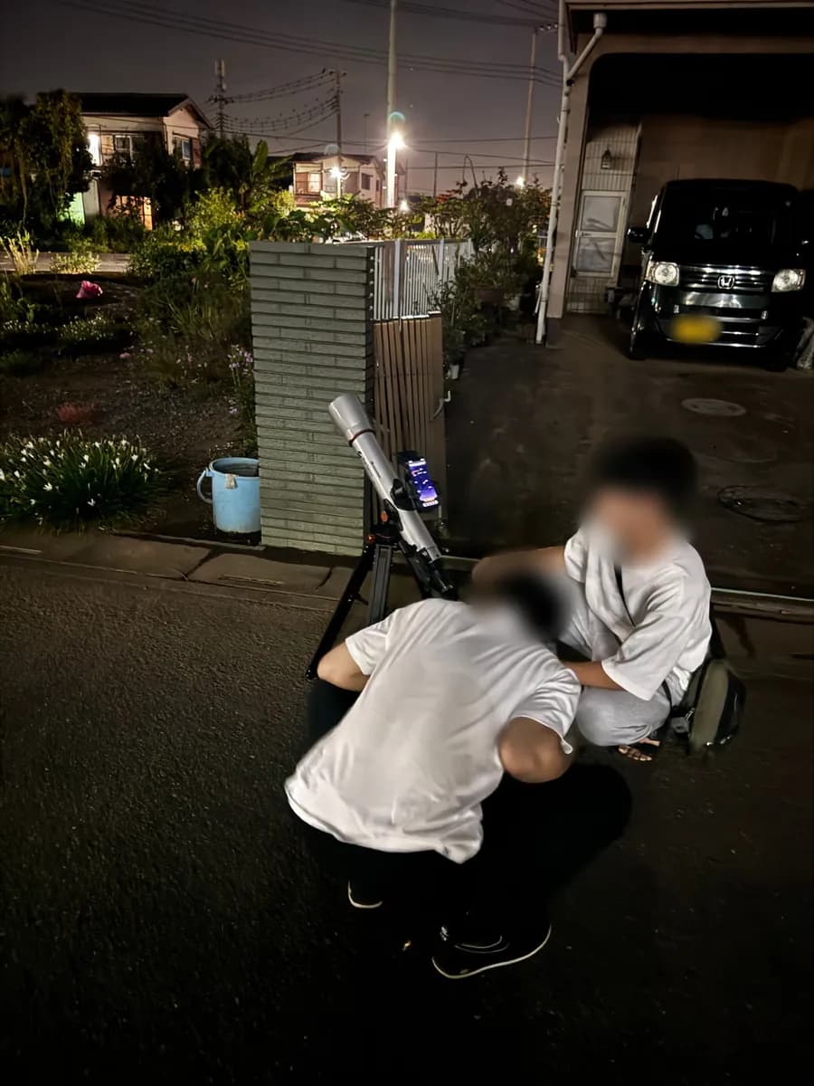 夜の住宅街で、道ばたに立てたStarSense Explorer LT 70AZを、編集部の2人がのぞき込んでいる(人物の顔と車のナンバーはぼかしています)