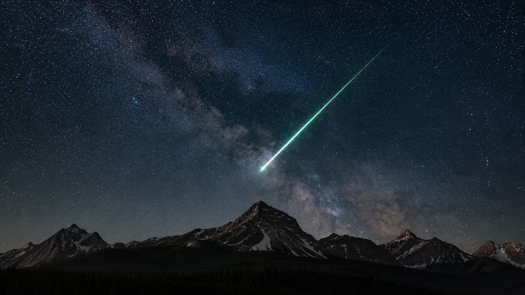 天の川と無数の星が見える山の夜空を、緑白色の光跡を残して横切る一つの流れ星