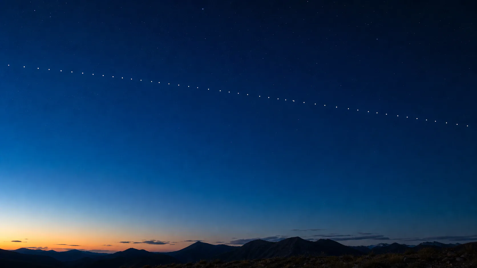 薄明の空を、一列に連なって進むスターリンク衛星の光点