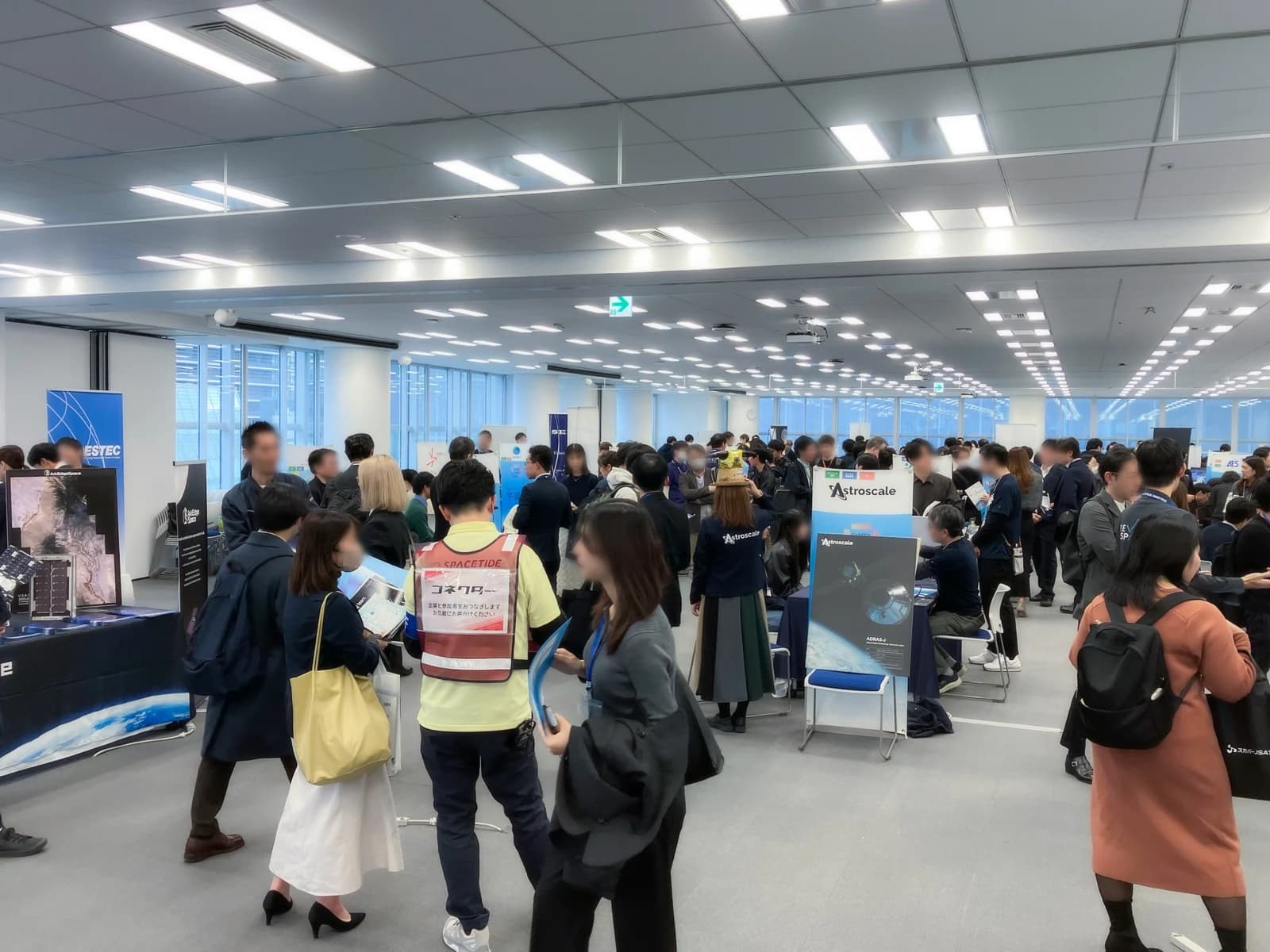 宇宙関連企業のブースが並ぶ会場で、多くの来場者が担当者と話している様子