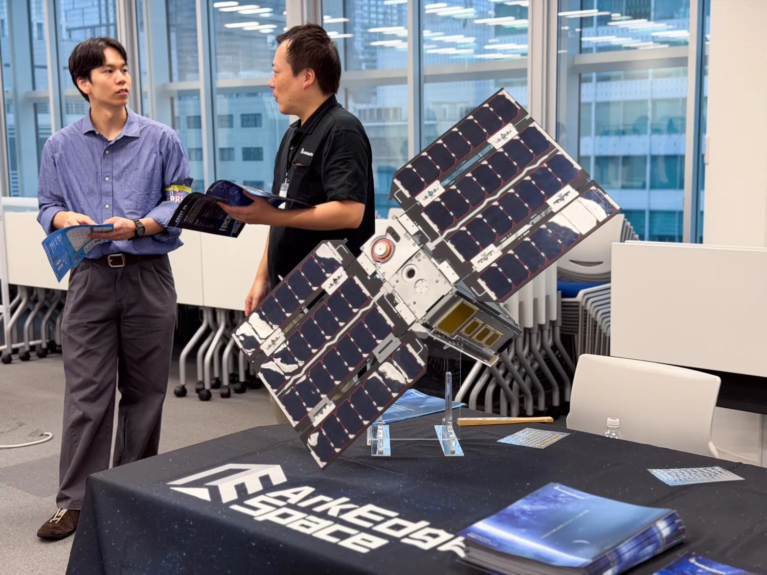 SPACETIDE Career Connect 2026の企業ブースに展示された超小型衛星の模型と、その前で話す担当者と参加者